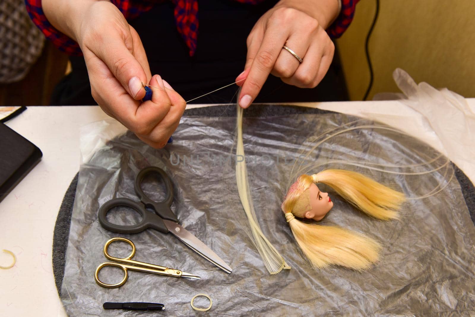 female hands and homemade tool on the table, how to make a hairstyle for a doll, hobby concept.