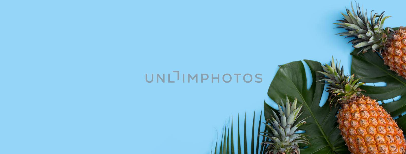 Top view of fresh pineapple with tropical palm and monstera leaves on blue table background.