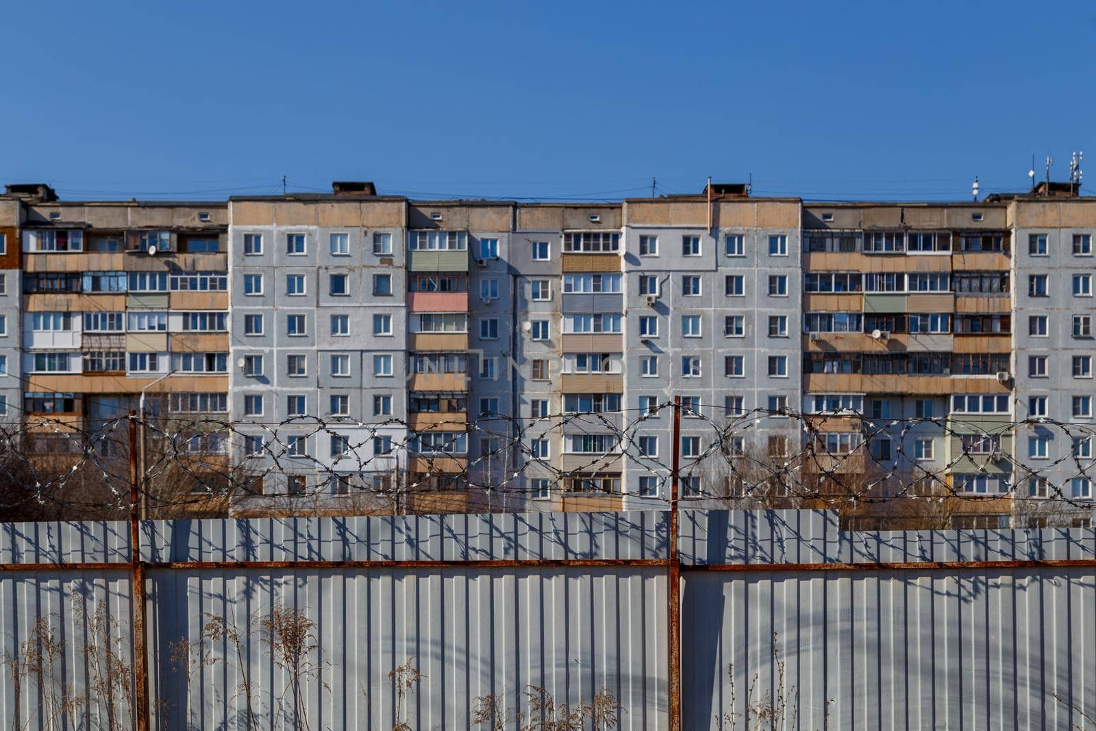 residential multi-storey building behind a fence with barbed wire at daylight, the concept of imprisonment, restriction of freedom, quarantine.