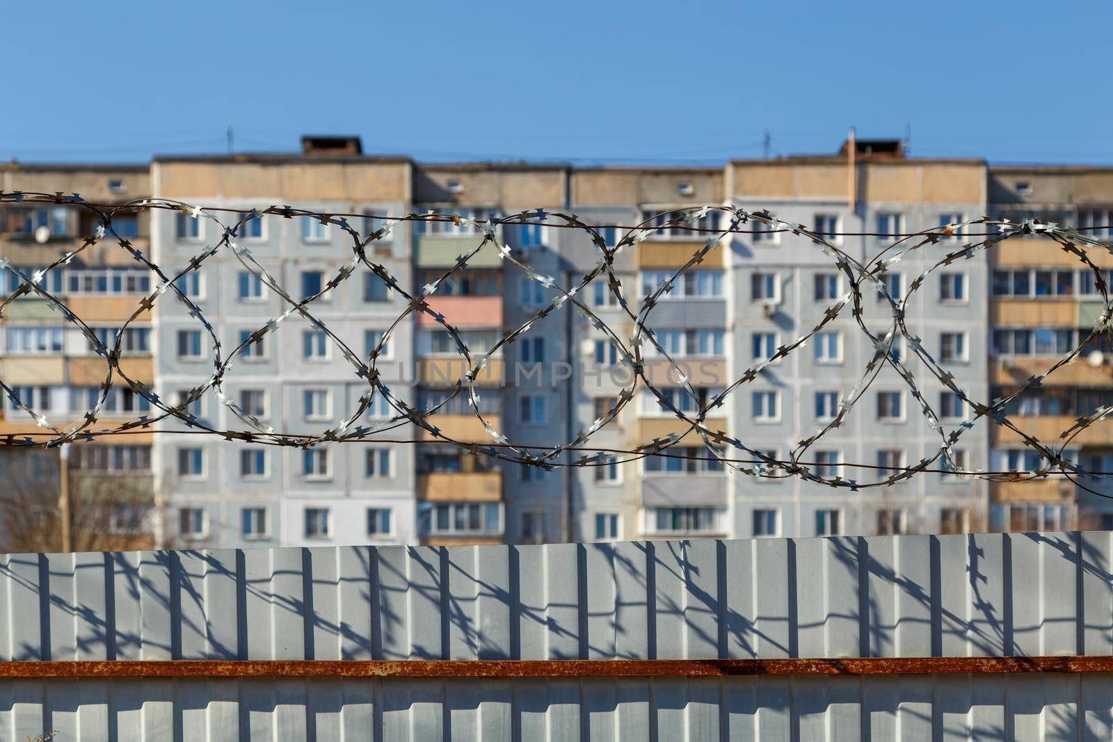 residential multi-storey building behind a fence with barbed wire at daylight, the concept of imprisonment, restriction of freedom, quarantine.