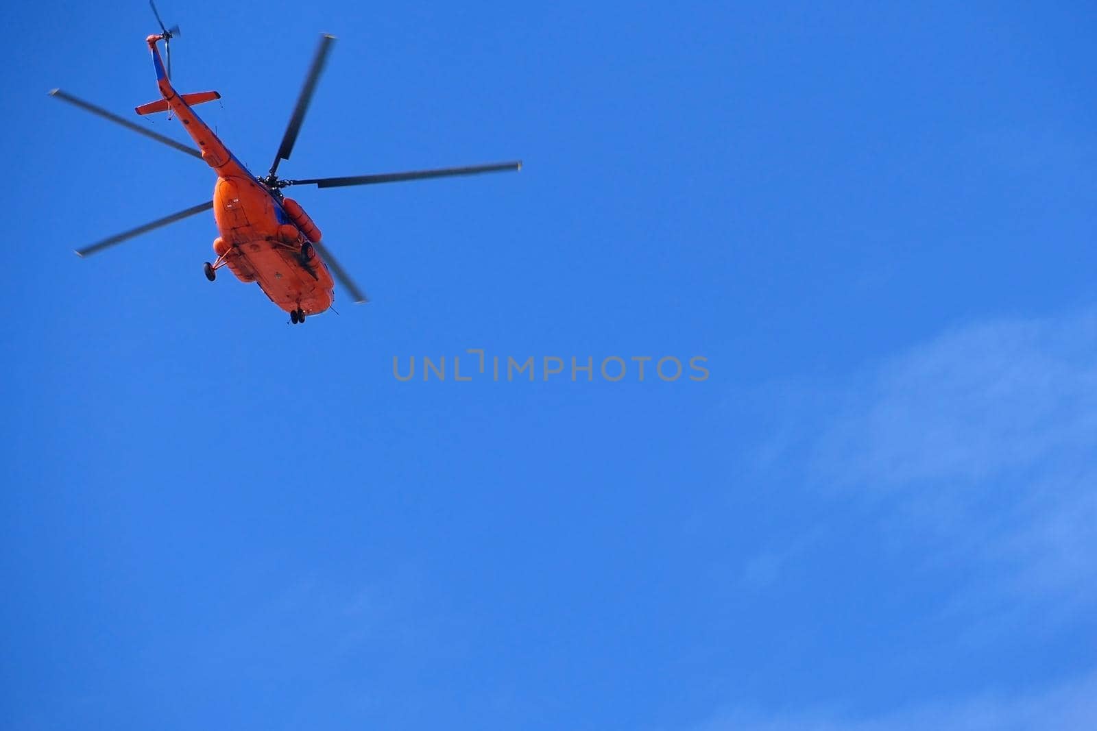 A red helicopter flies high in the blue sky, Aviation. High quality photo