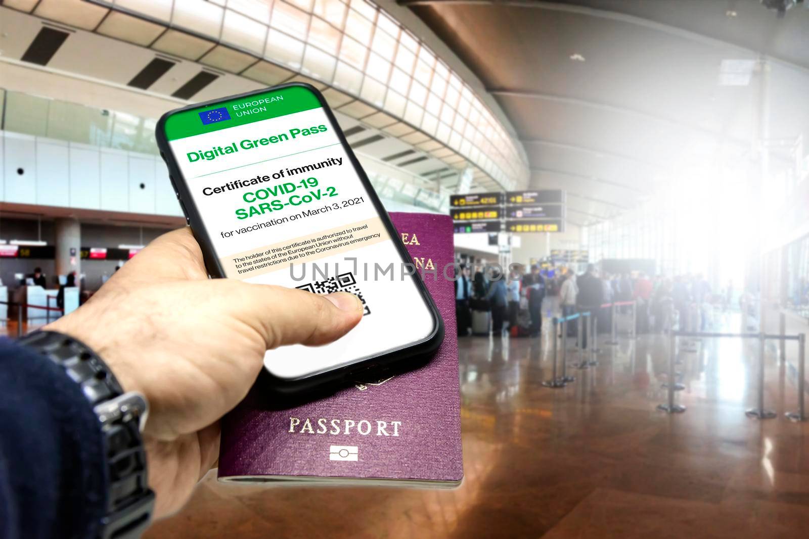 Male hand holding a phone with the European Union vaccination certificate on the screen and a traditional passport inside an airport. Immunity from Covid-19. Travel without restrictions.