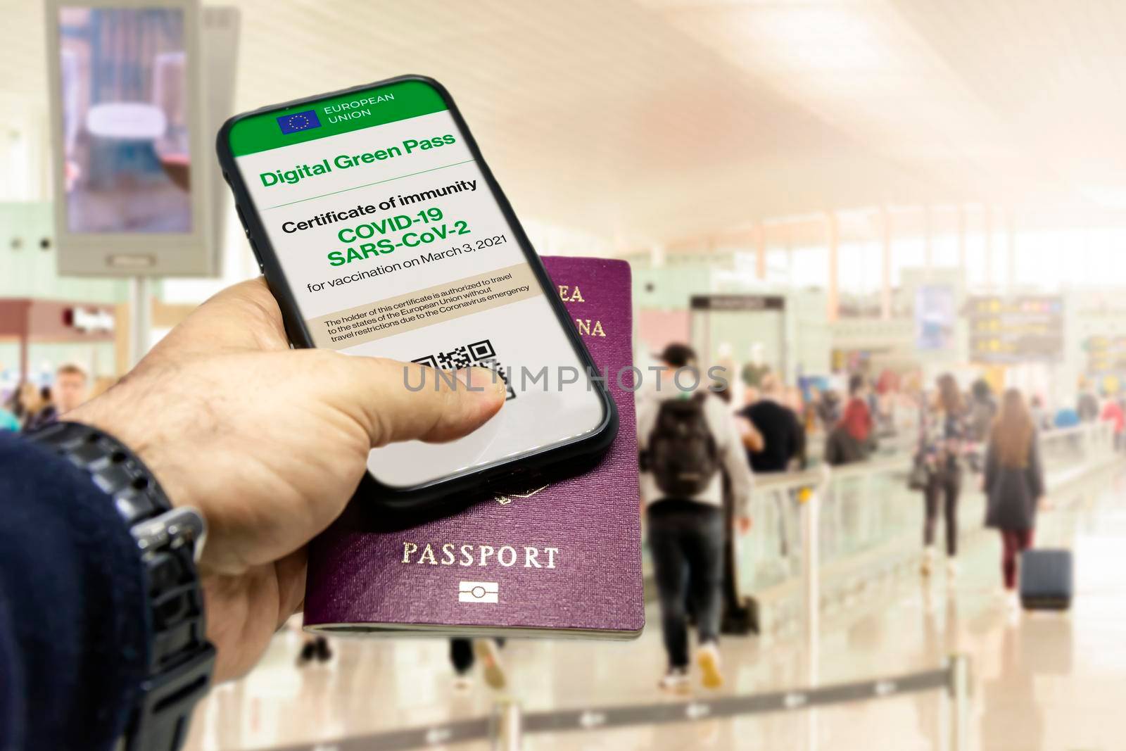 Male hand holding a phone with the European Union vaccination certificate on the screen and a traditional passport inside an airport by rarrarorro