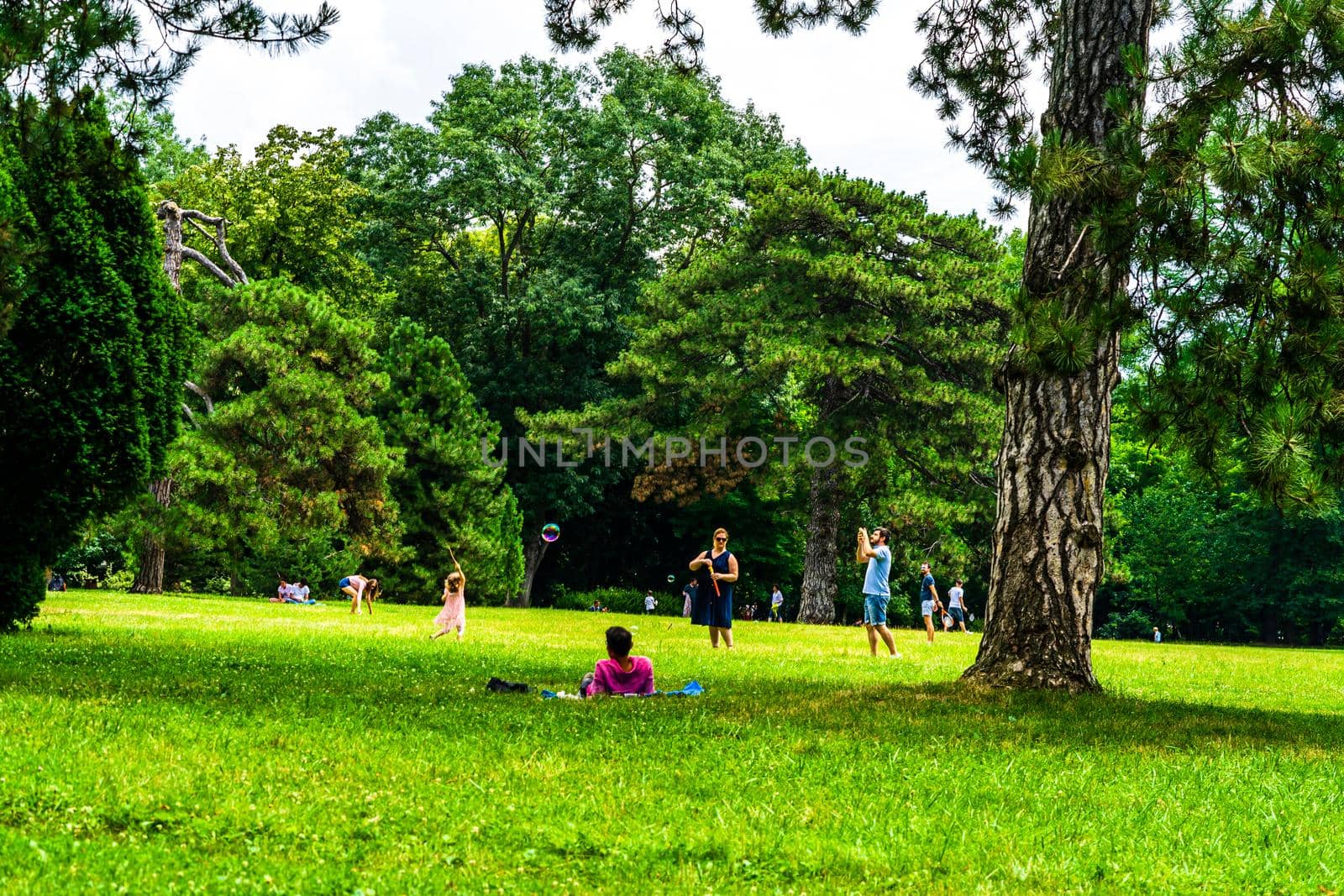 Mother making soap bubbles for herlittle daughter, people having picnic relaxing and having fun during coronavirus crisis in park and gardens of the domain from Mogosoaia in Bucharest, Romania, 2020.