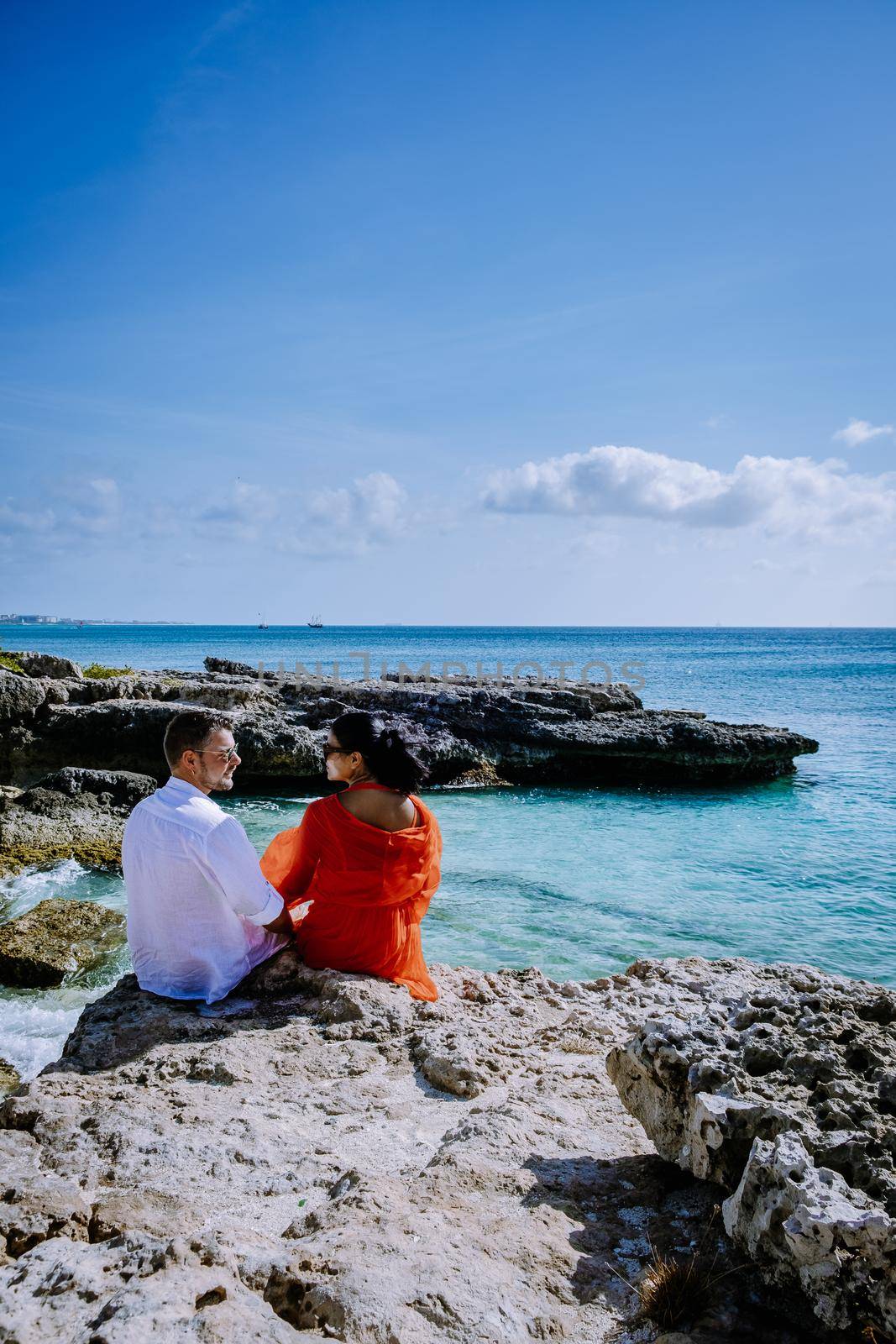 Boca Catalina Beach Aruba, rocks and cliffs and blue ocean Aruba, couple men and woman sitting on a rock watching together