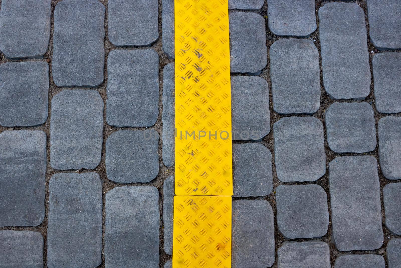 The texture of gray paving slabs with a yellow stripe on the street, a promising view. Cement brick square stone floor background. Sidewalk pavement pattern.