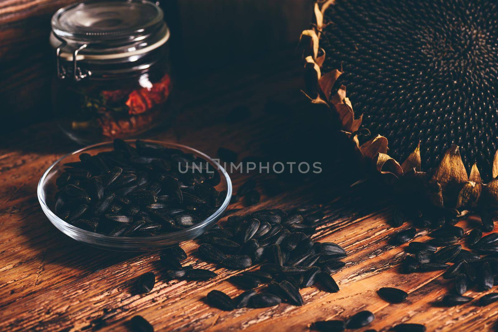 Roasted seeds on the glass saucer and dried sunflower over old wooden surface