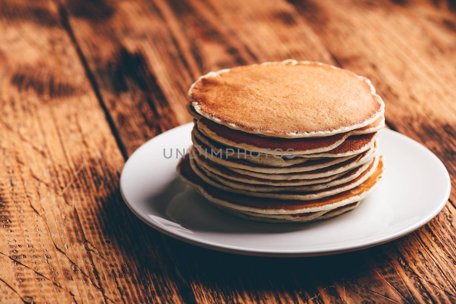 Stack of american pancakes on white plate over wooden table