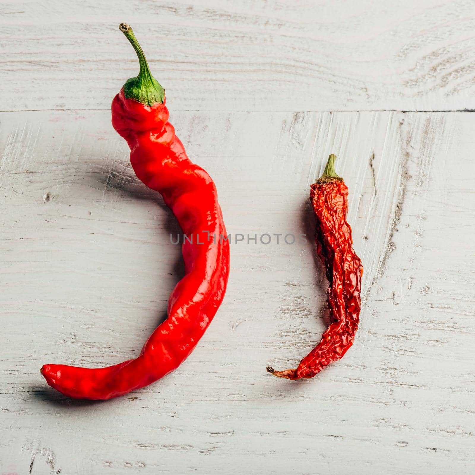 Two red chili peppers, fresh and dry, over wooden background