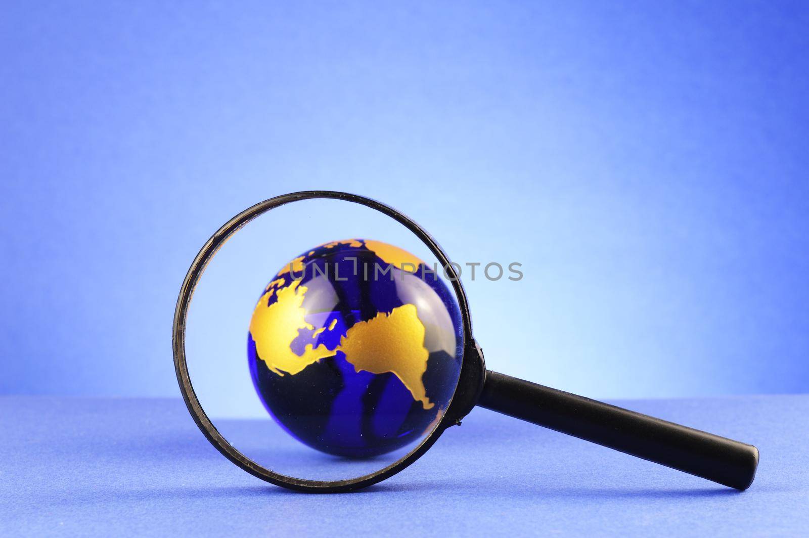 A magnify glass focused on a blue earth globe for searching world views concepts.