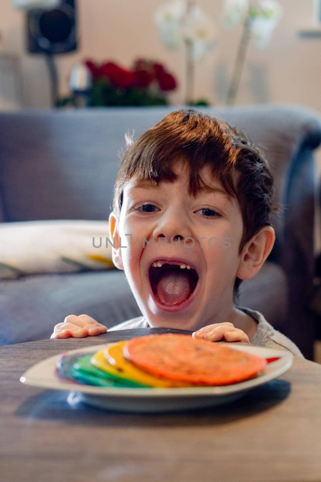 A cute blue-eyed boy looking at a plate of colorful pancakes with his mouth open