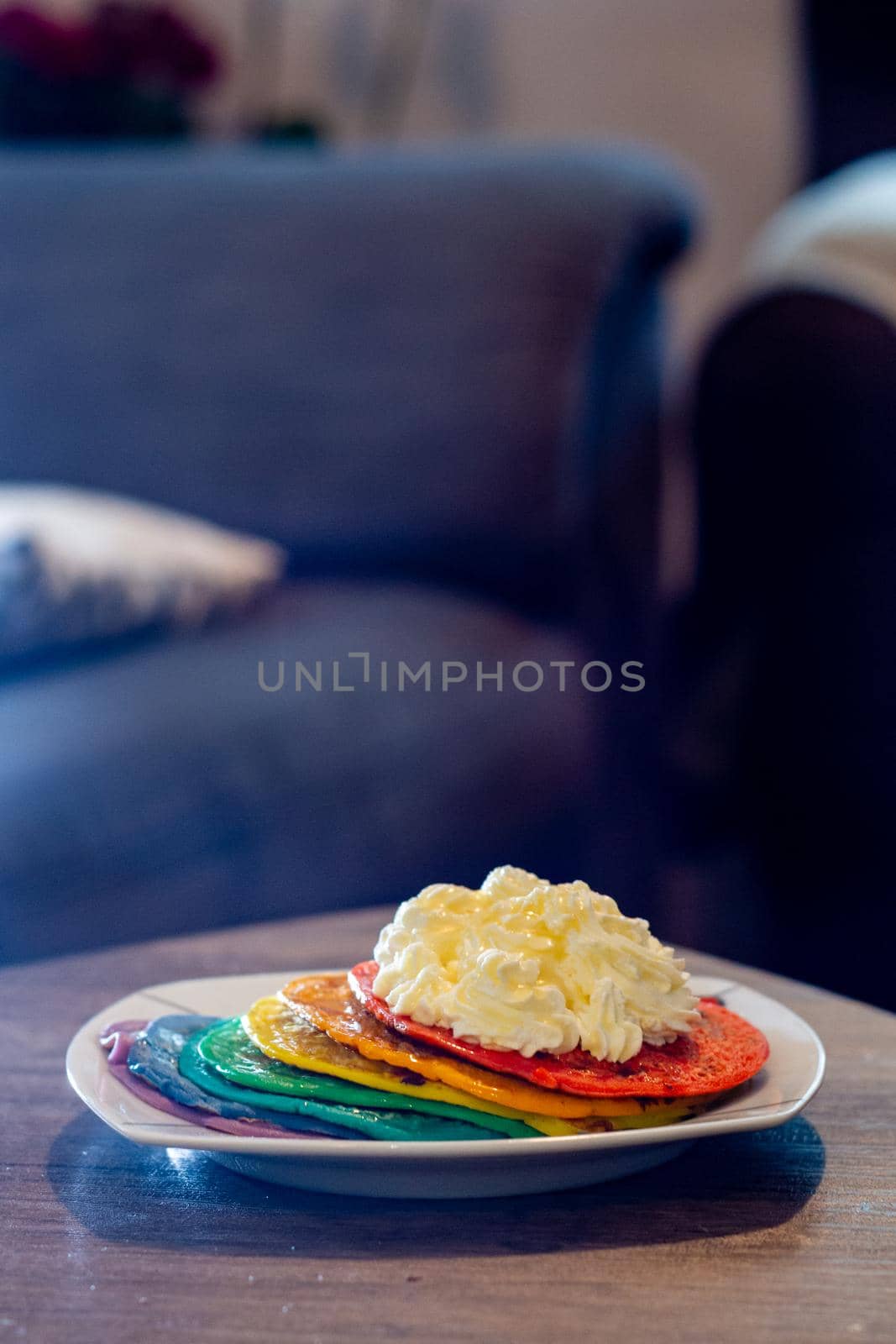 Close-up of a dish with rainbow colored pancakes with a dollop of whipped cream on a wood table in a living room