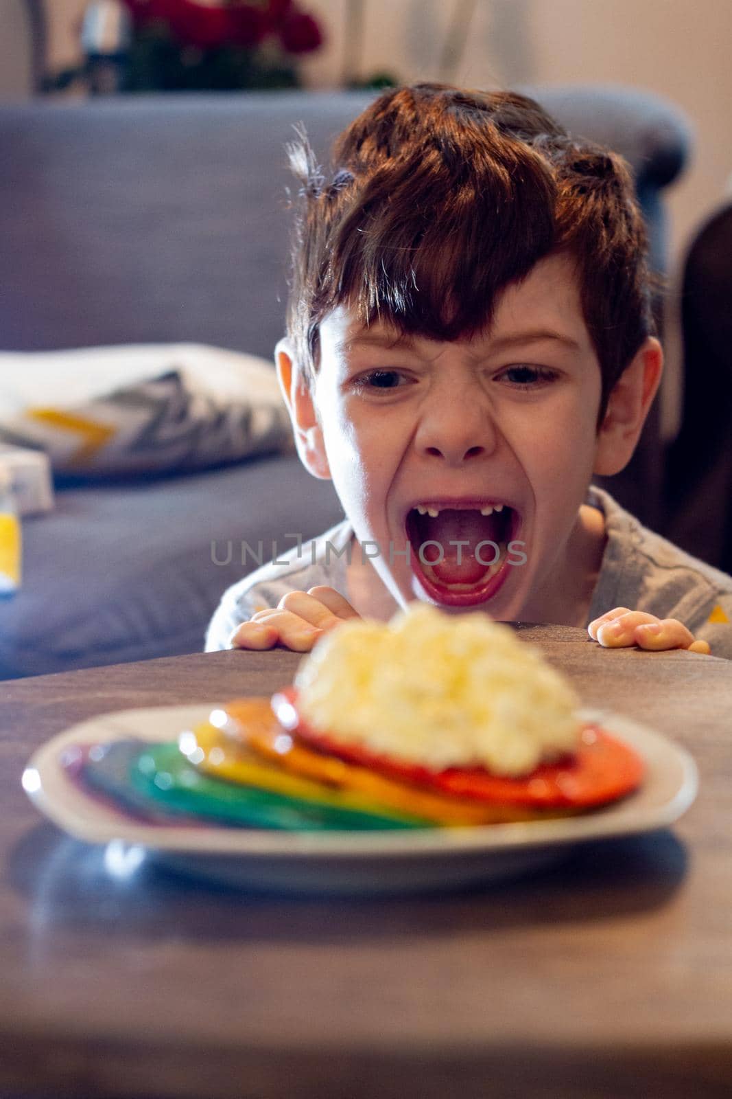 A plate of rainbow colored pancakes  with a dollop of cream on a table with a cute boy looking in the background