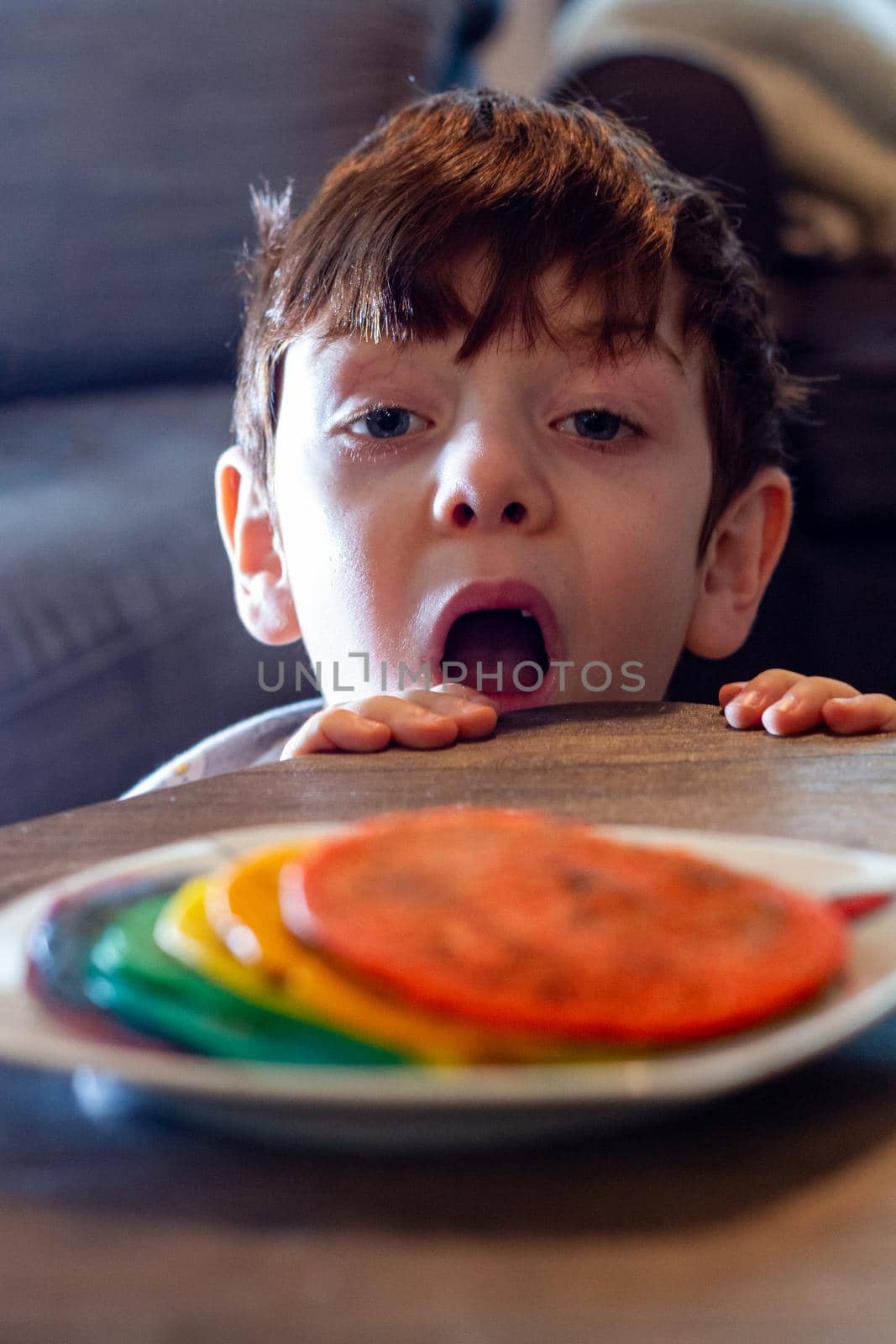 A cute blue-eyed boy looking at a plate of colorful pancakes with his mouth open