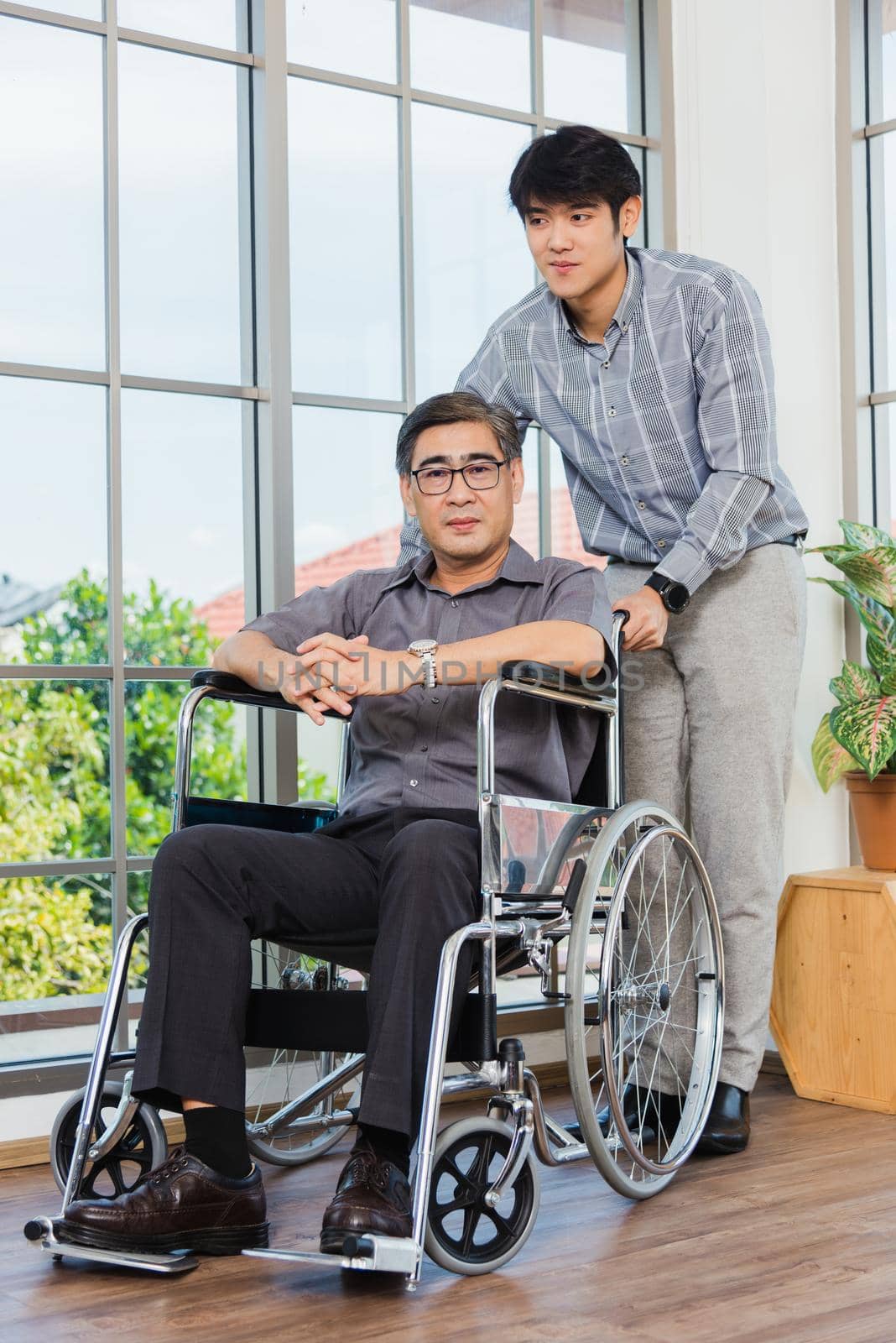 Asian senior disabled businessman in wheelchair discuss interacting together with the team in the office. The old man in a wheelchair and his young son talking to and comforting bound father