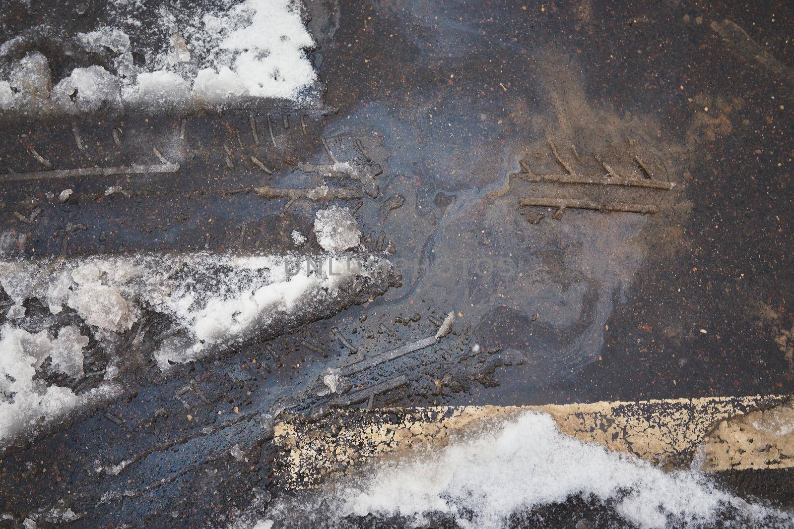 Tire tracks in the melting snow against the background of an oil spot on asphalt road