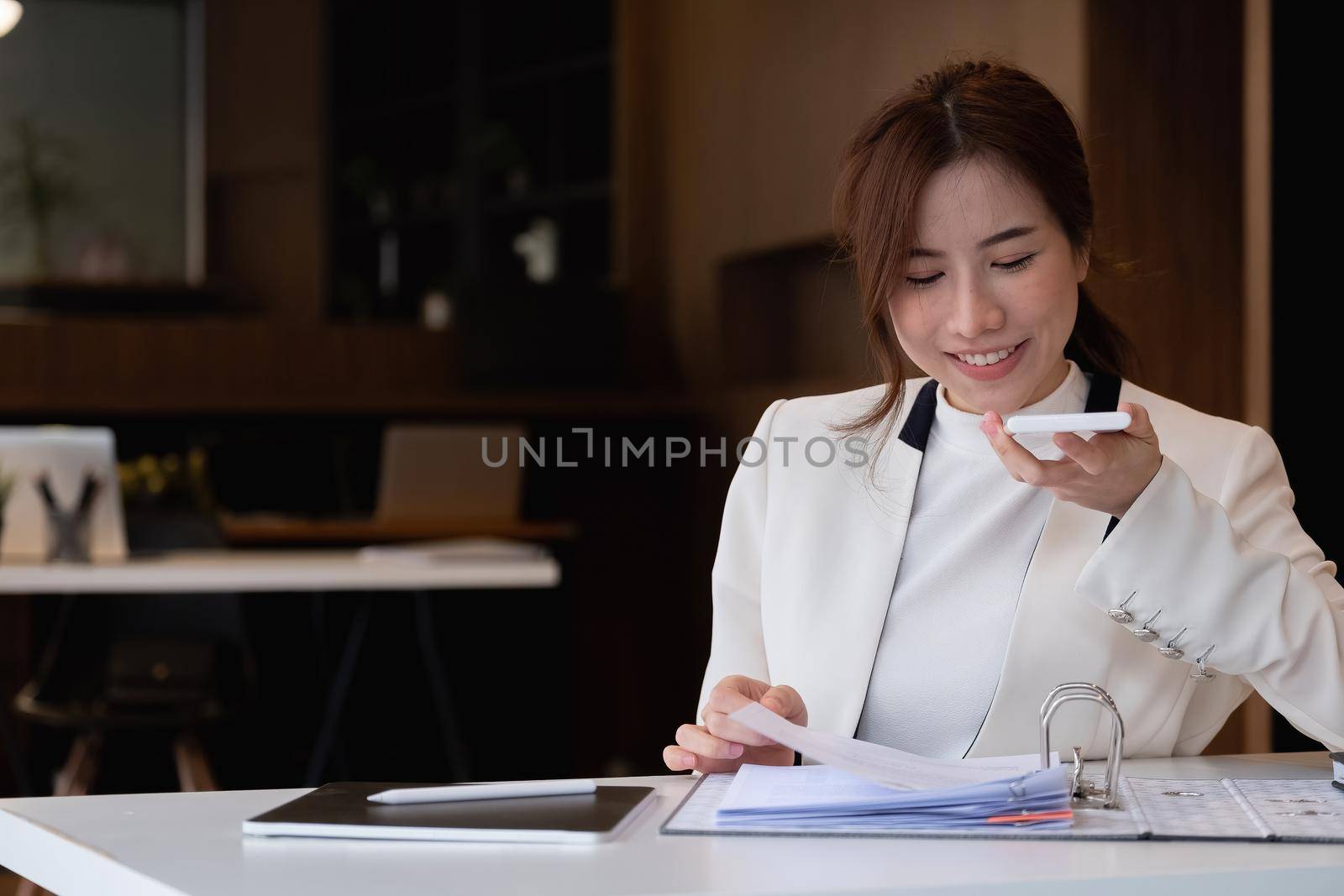 Young asian businesswoman beautiful charming smiling and talking on the mobile phone with speaker phone in the office by nateemee