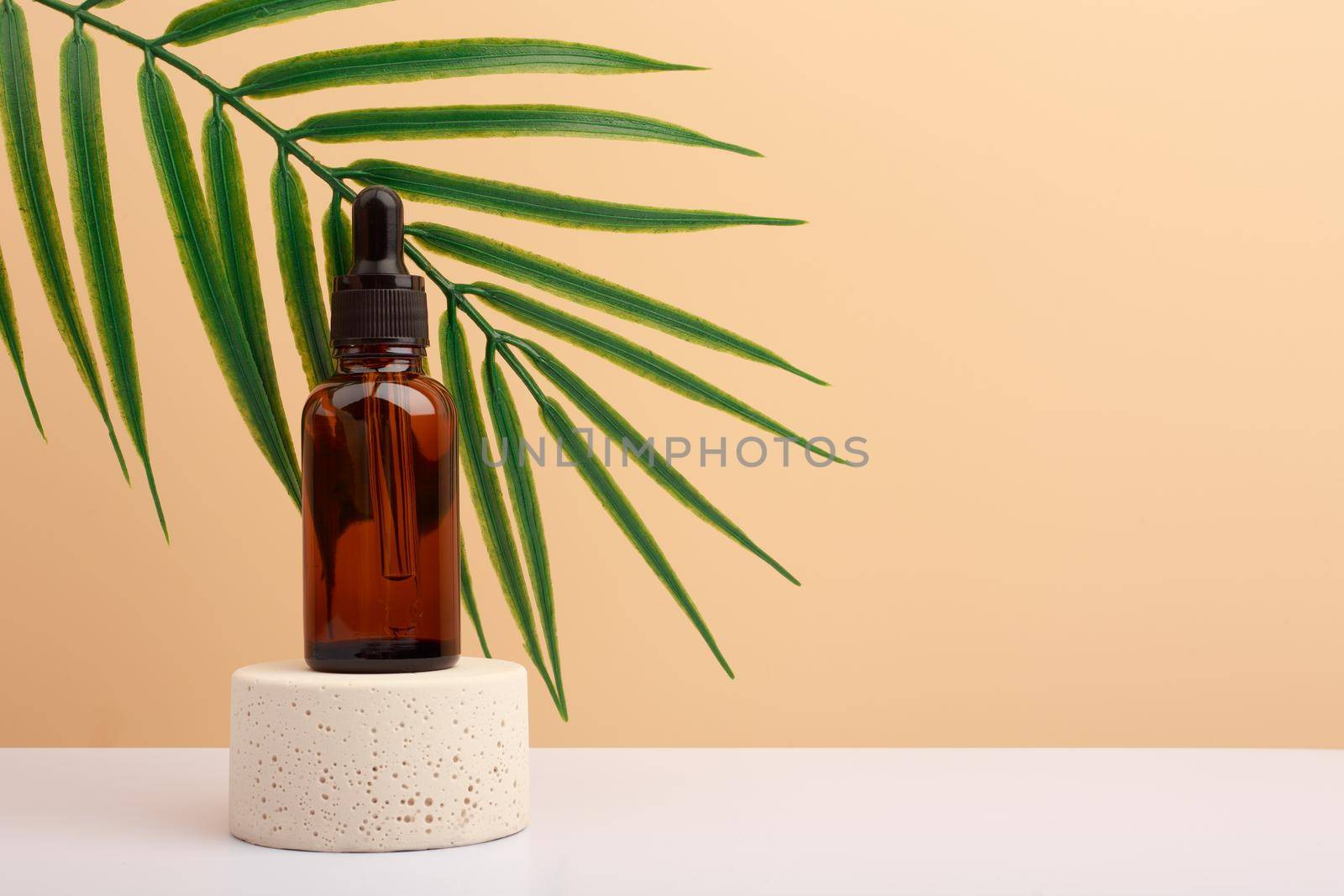 Skin serum on beige stone podium with palm leaf on white table against beige background with copy space. 