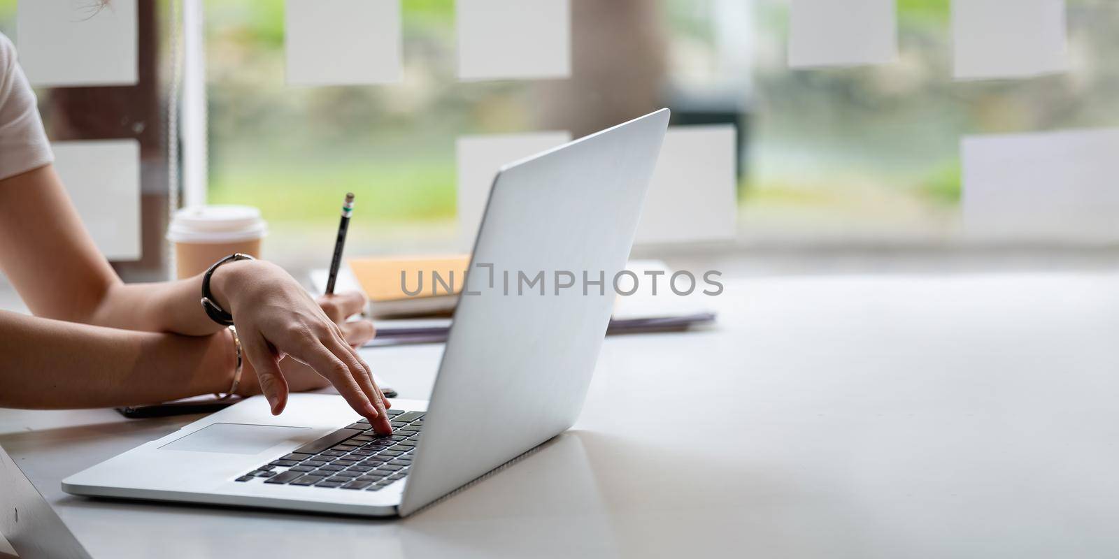 Cropped photo hand of woman writing making list taking notes in notepad working or learning online with laptop at home.