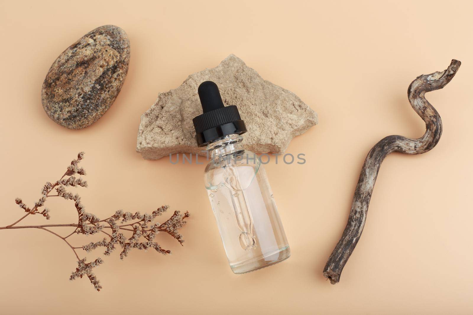 Selective focus, skin serum in transparent bottle with dry flower, stones and stick. Concept of organic beauty products by Senorina_Irina