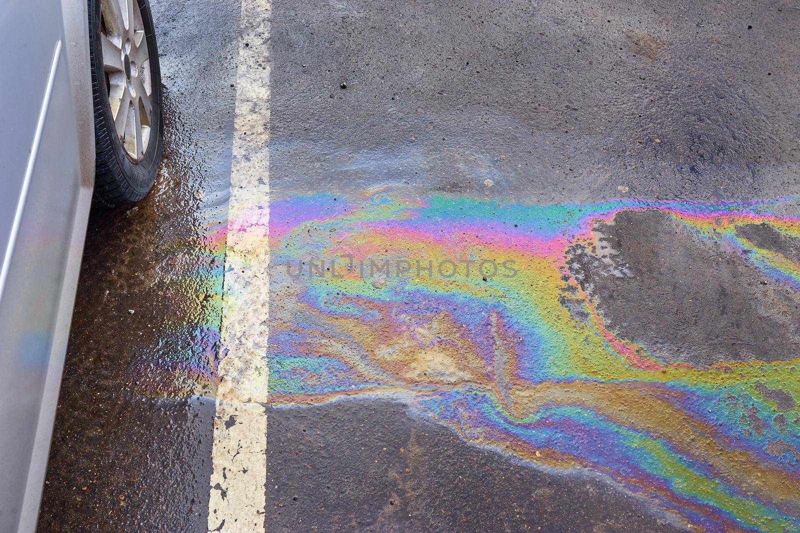 Colorful gas stain on wet asphalt. Oil stain or gasoline caused by a leak under a car. Environmental pollution concept.