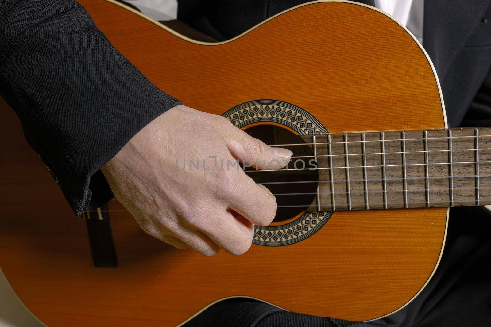 A man sitting and playing classic wooden guitar close up