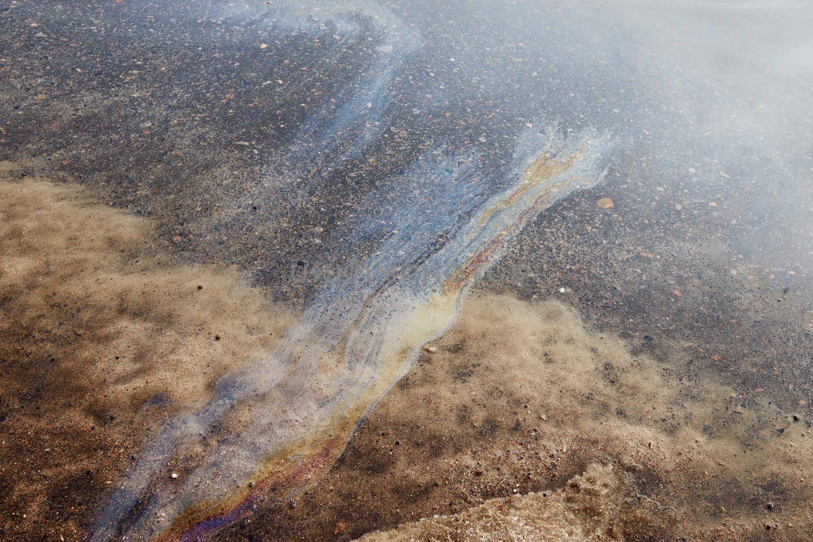 Rainbow gasoline stain on the asphalt. Snow melts after winter