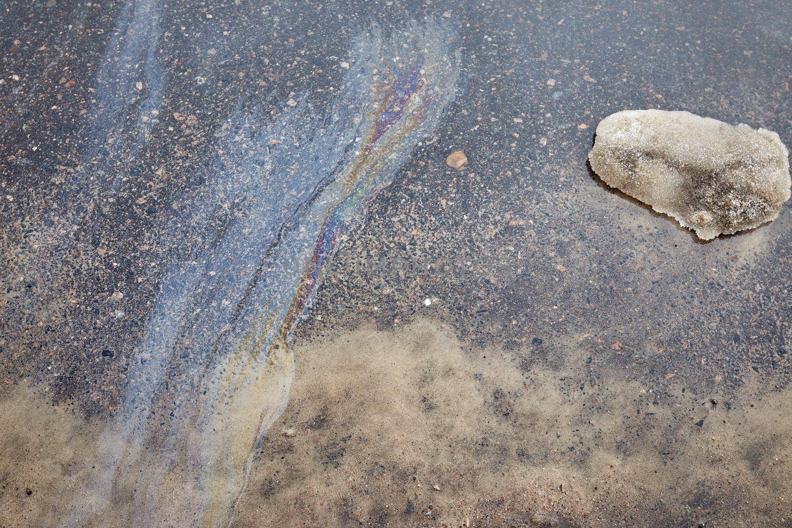 Rainbow gasoline stain on the asphalt. Snow melts after winter