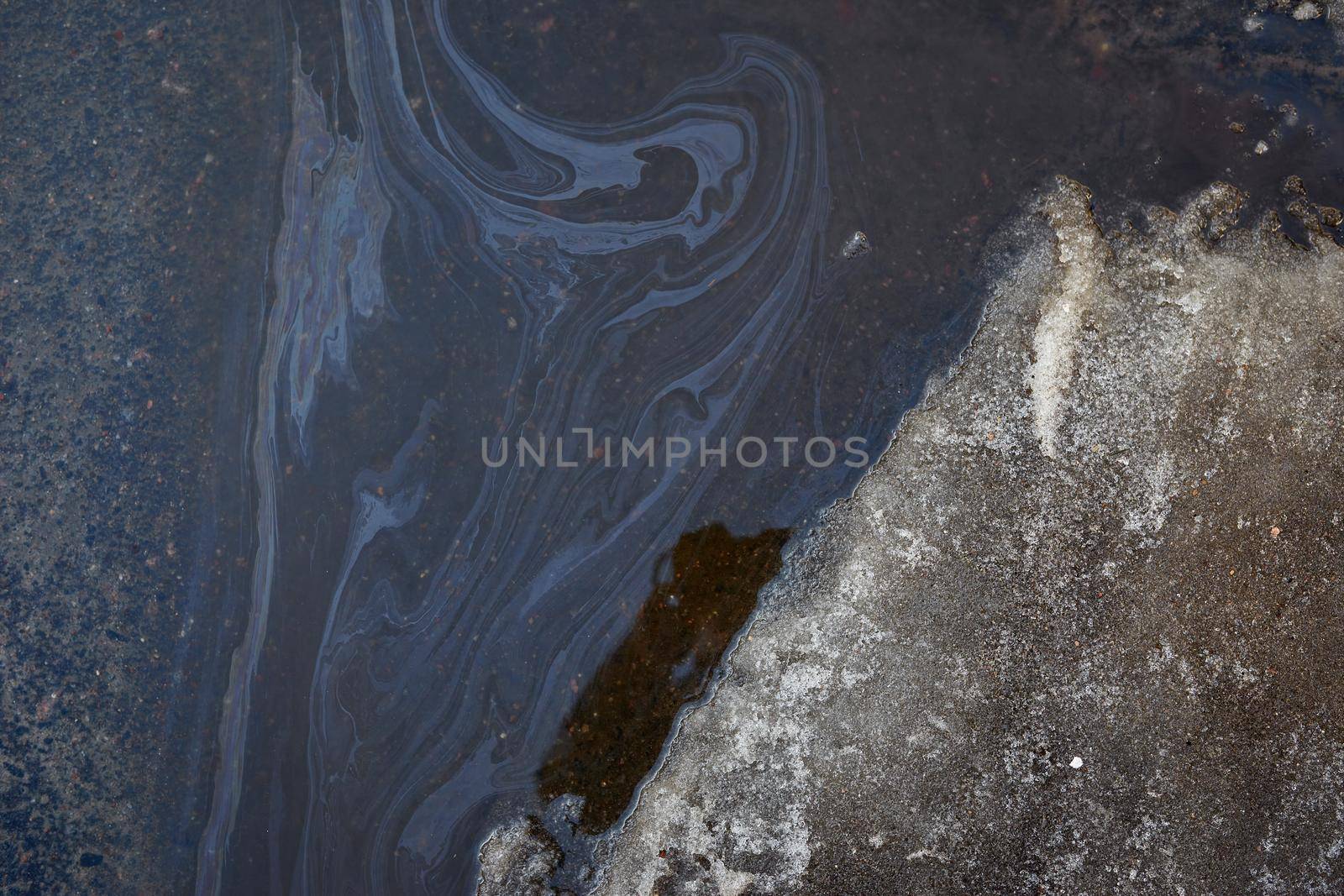 Rainbow spots of gasoline and gas near the car. Snow melts after winter