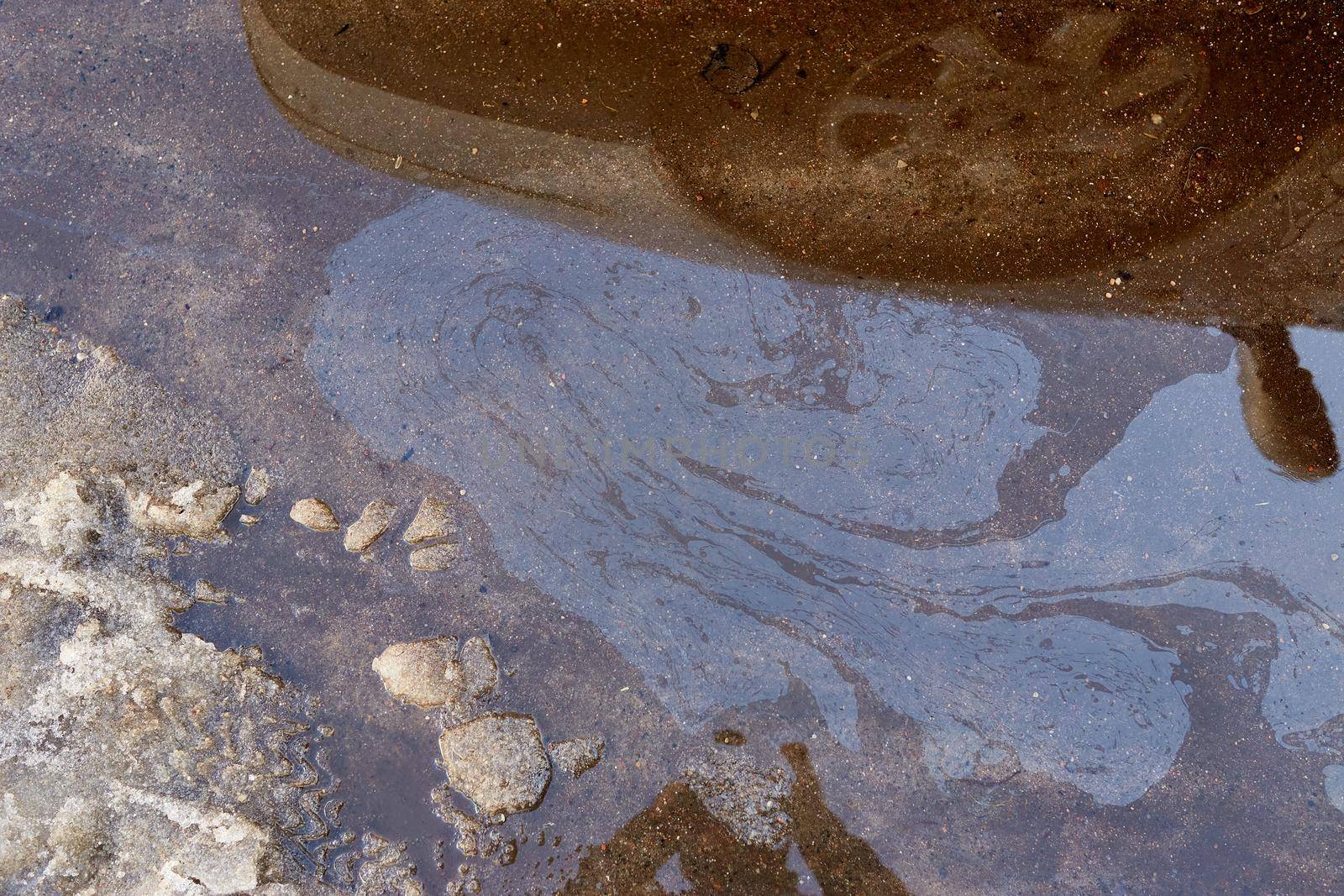 Rainbow spots of gasoline and gas near the car. Snow melts after winter