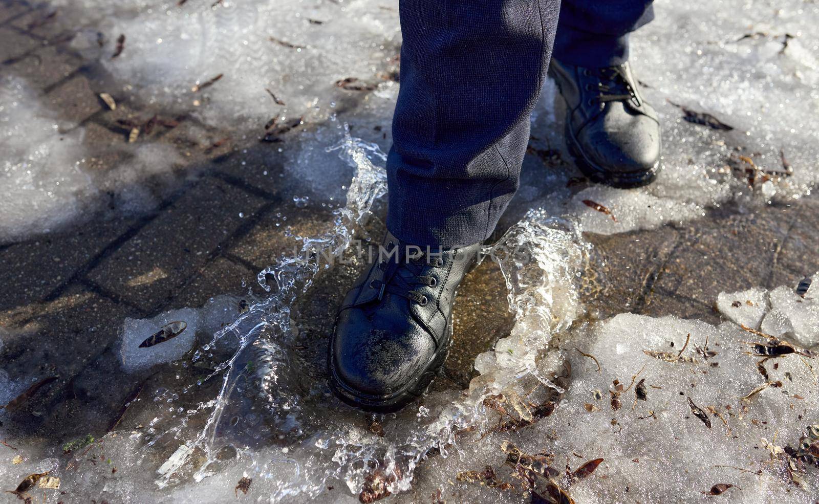 Male feet in shoes walk on a puddle of melted snow. Selective focus