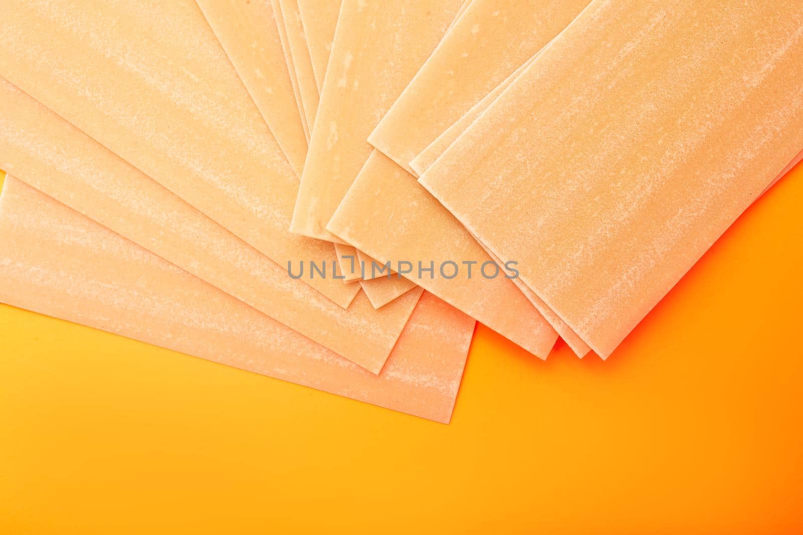 Raw lasagna pasta on orange background fanned out