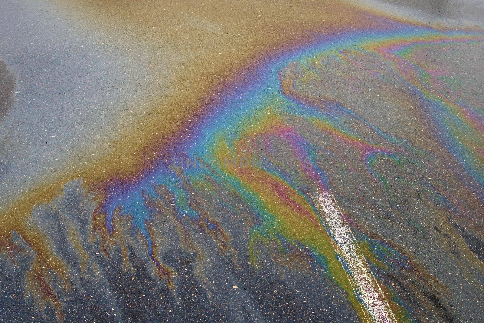 Gasoline flows on the asphalt surface in a car park. Iridescent stains of gasoline.