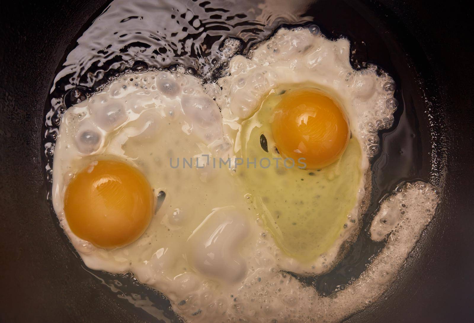 chicken eggs in a cast iron pan close-up, breakfast, two eggs with yellow yolks are fried on the stove