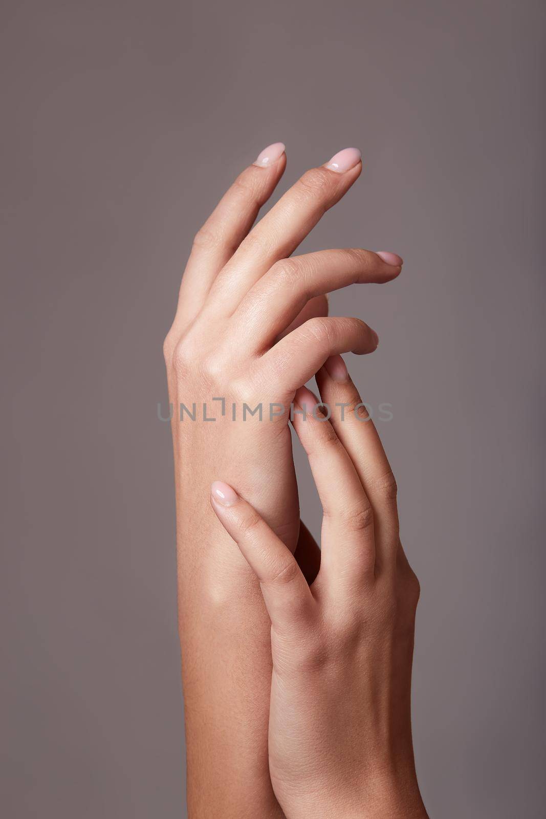 Closeup image of beautiful woman's hands with light pink manicure on the nails on gray background.
