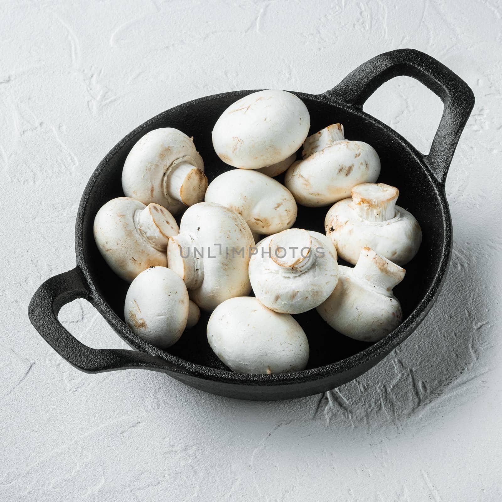 Mushroom champignon, in cast iron frying pan, on white stone surface, square format by Ilianesolenyi