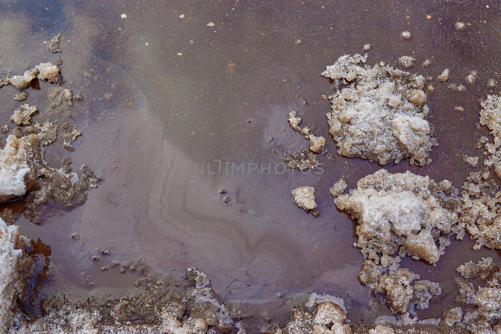 Rainbow stains from gasoline and oil on the asphalt surface in winter.