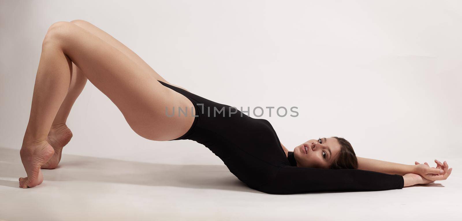 Young woman with athletic body lies on her back doing exercises by AliaksandrFilimonau