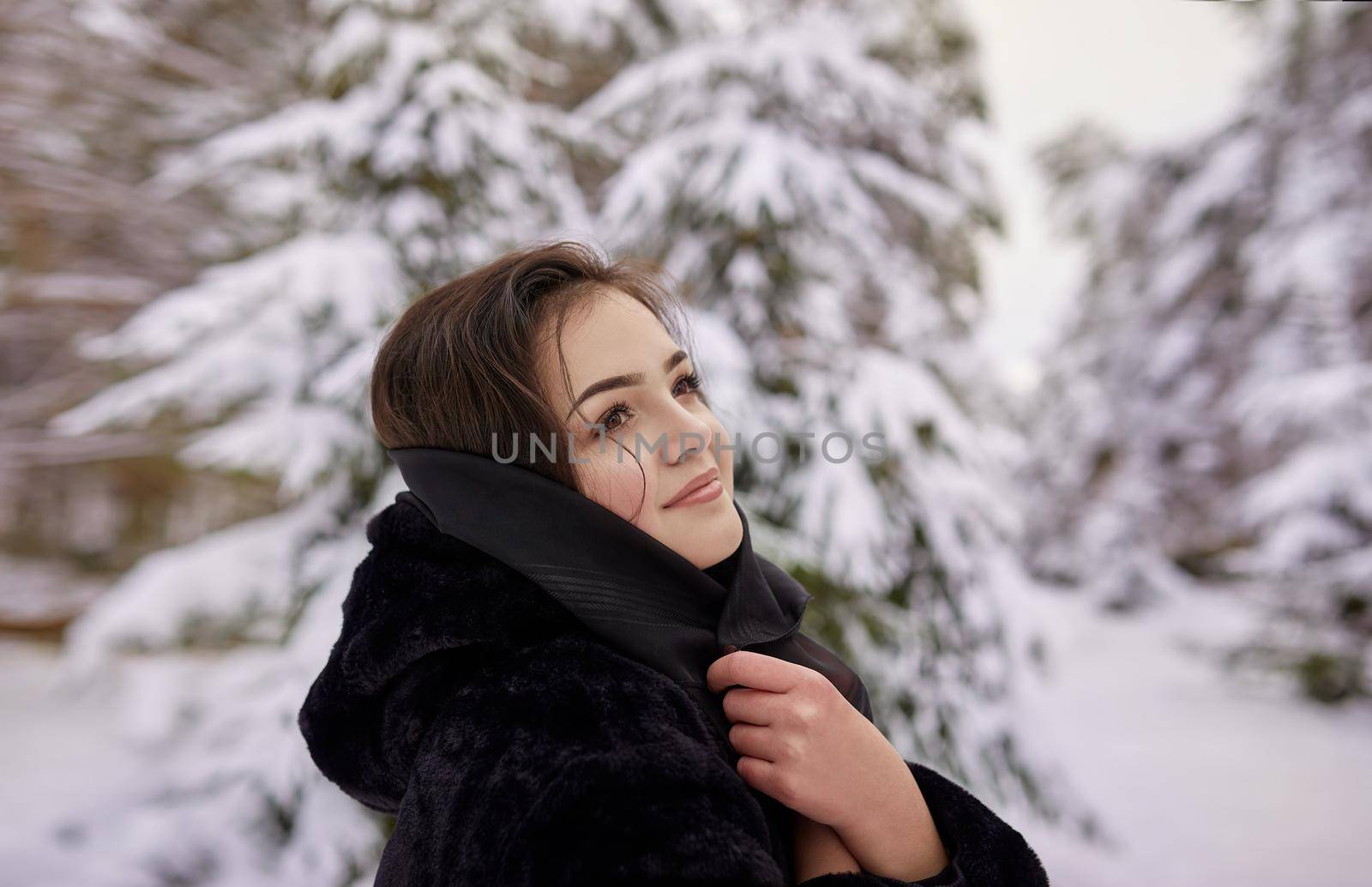 close up winter portrait of dreamy young woman walking in snowy forest with trees on background