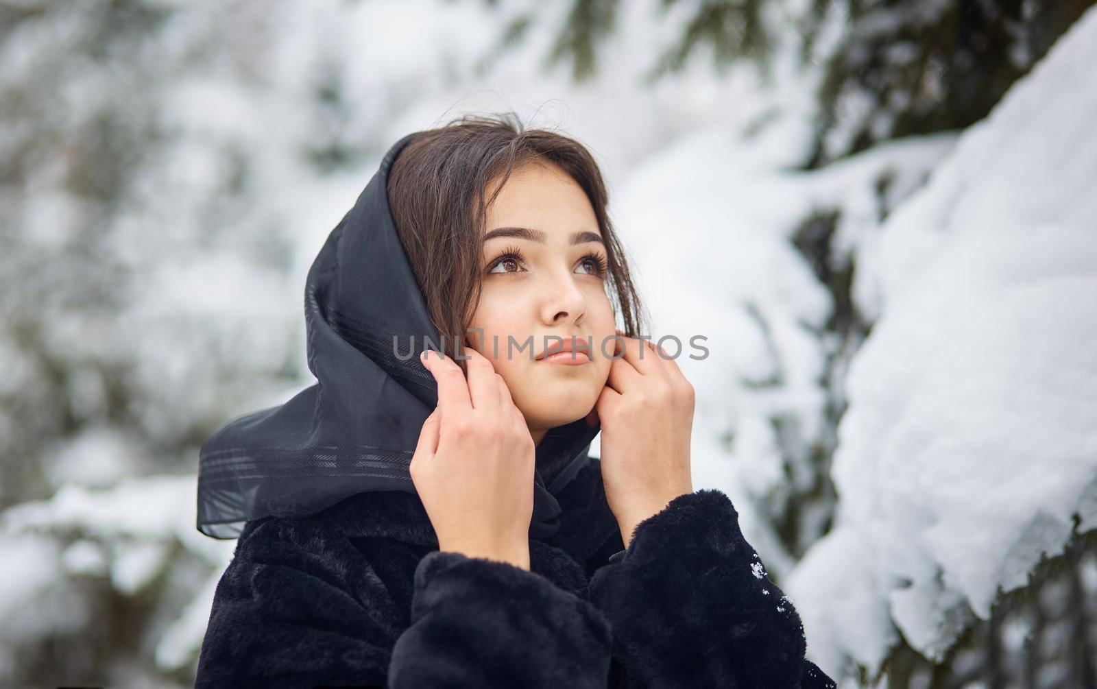 close up winter portrait of dreamy young woman walking in snowy forest with trees on background