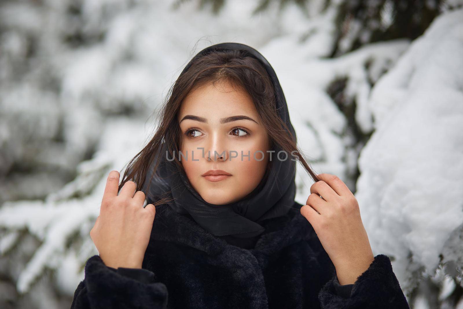 close-up winter portrait of dreamy young woman in snowy forest with trees on background