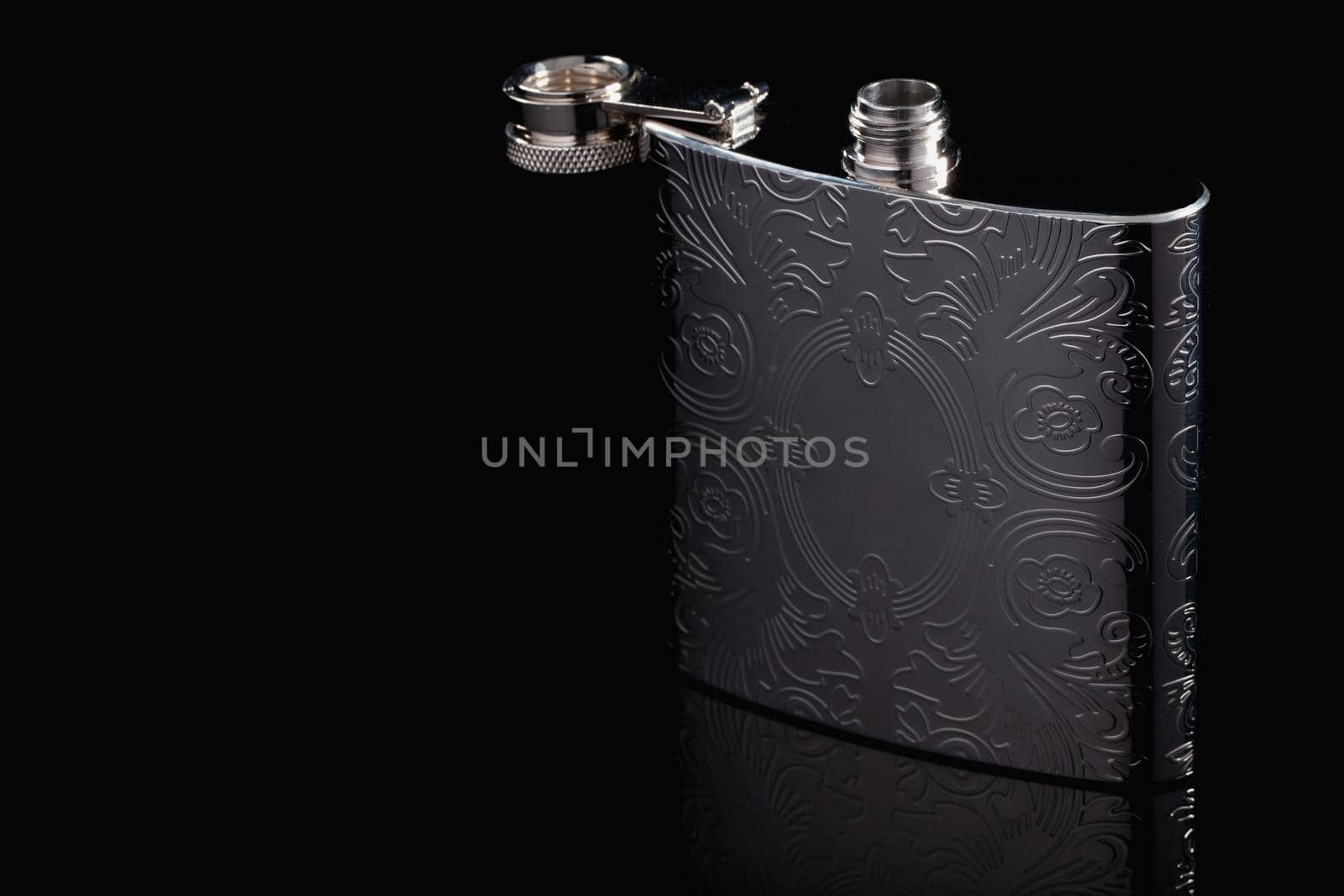 Stainless hip flask on the black glass table. Flask for alcohol. Lifestyle and travel.