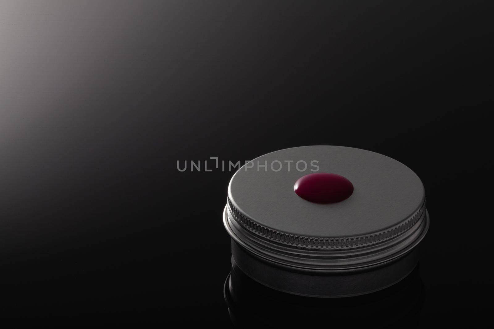 Silver metal containers for cosmetics and a drop of blood isolated on the black glass desk.