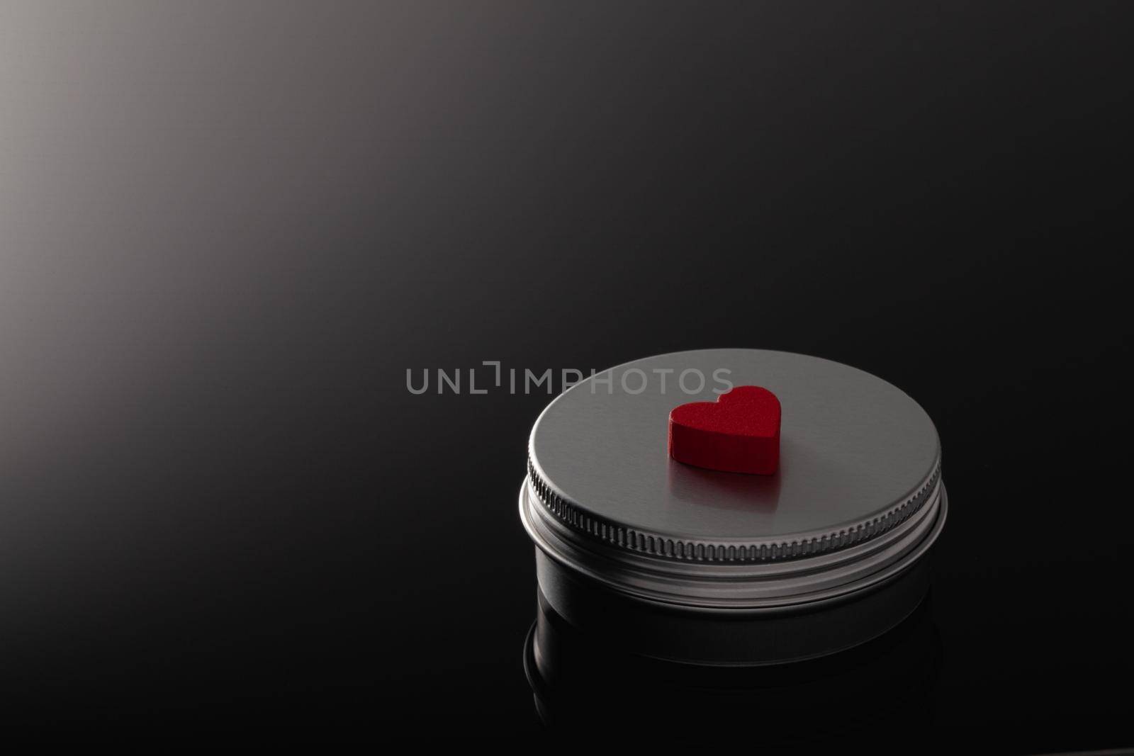 Silver metal containers for cosmetics and a red heart isolated on the black glass desk.