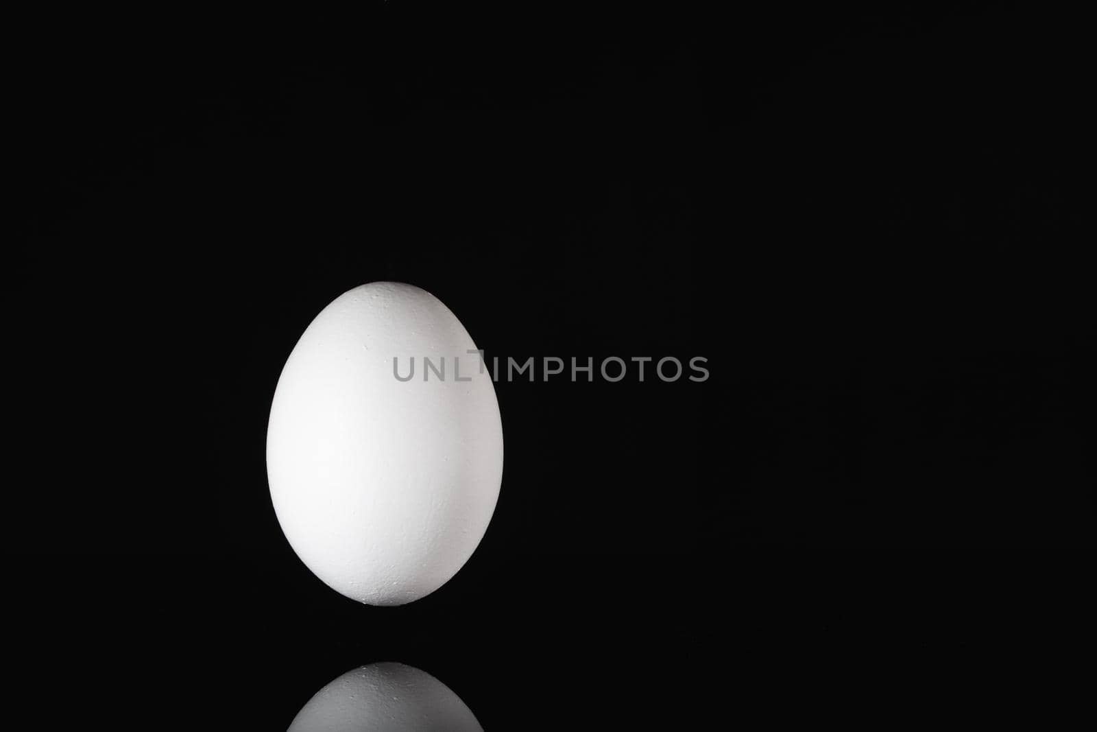 White egg levitating over a black glass table in the dark room.