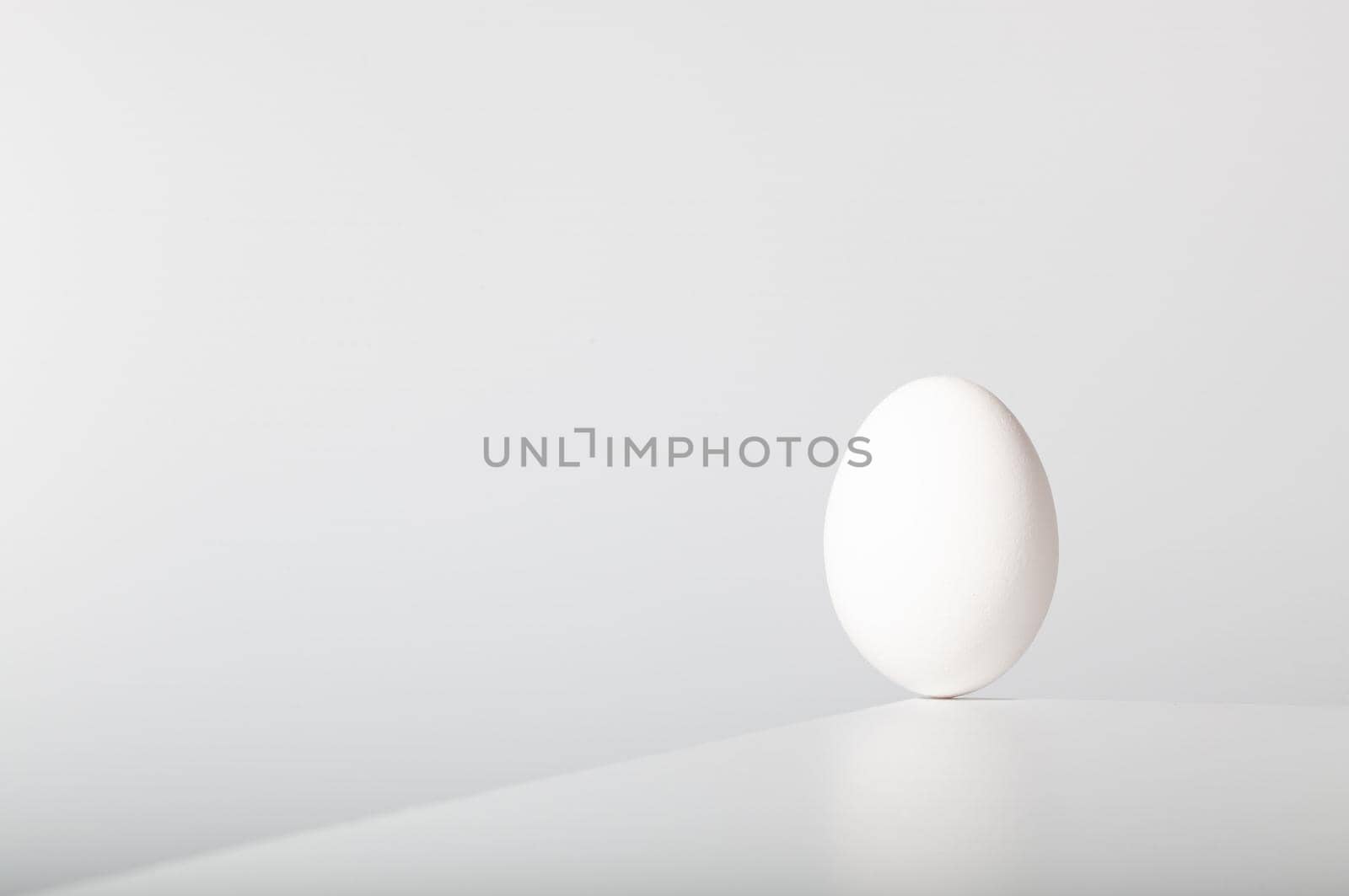 White egg balances on the edge of the white table.