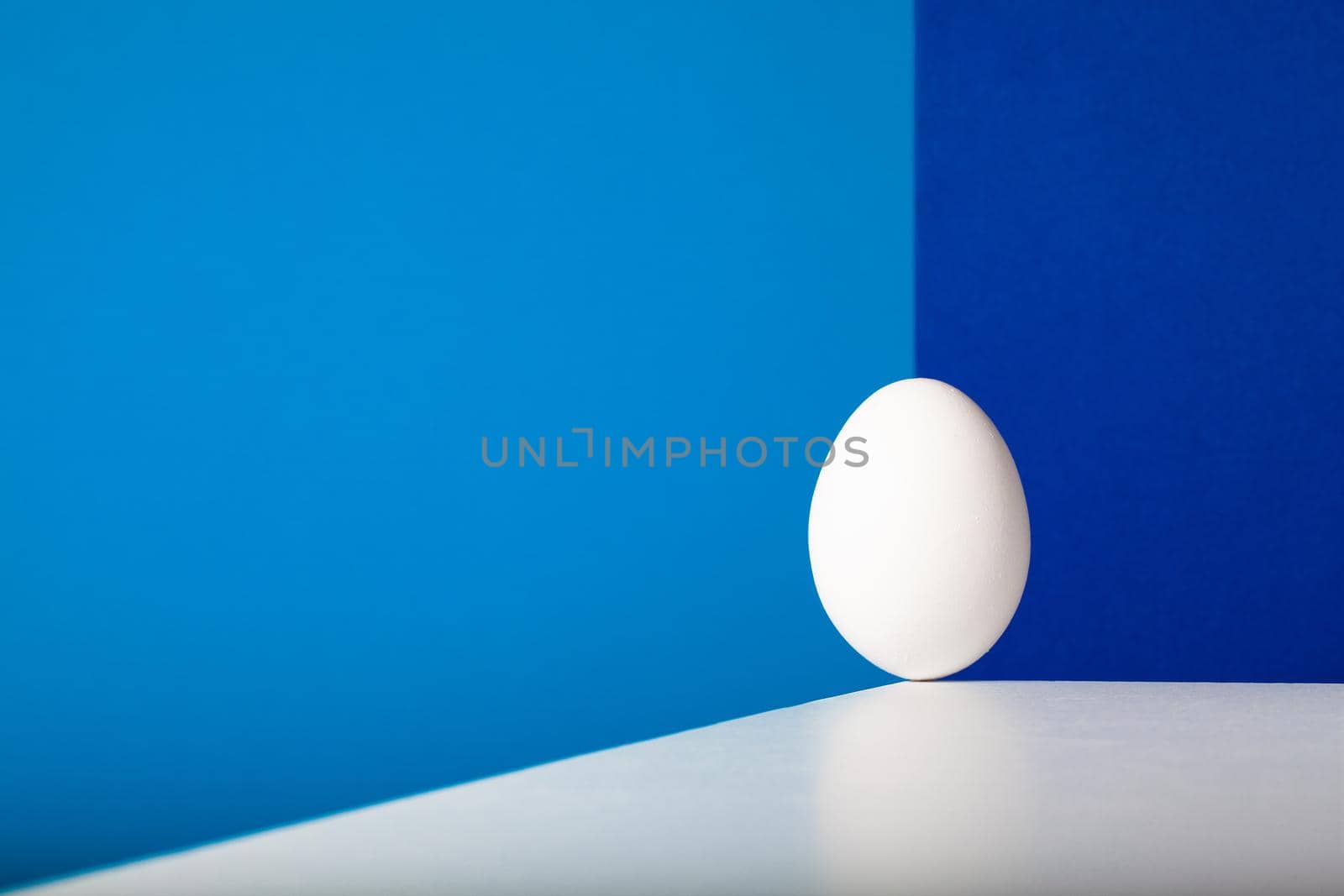White egg balances on the edge of the white table in the blue room.