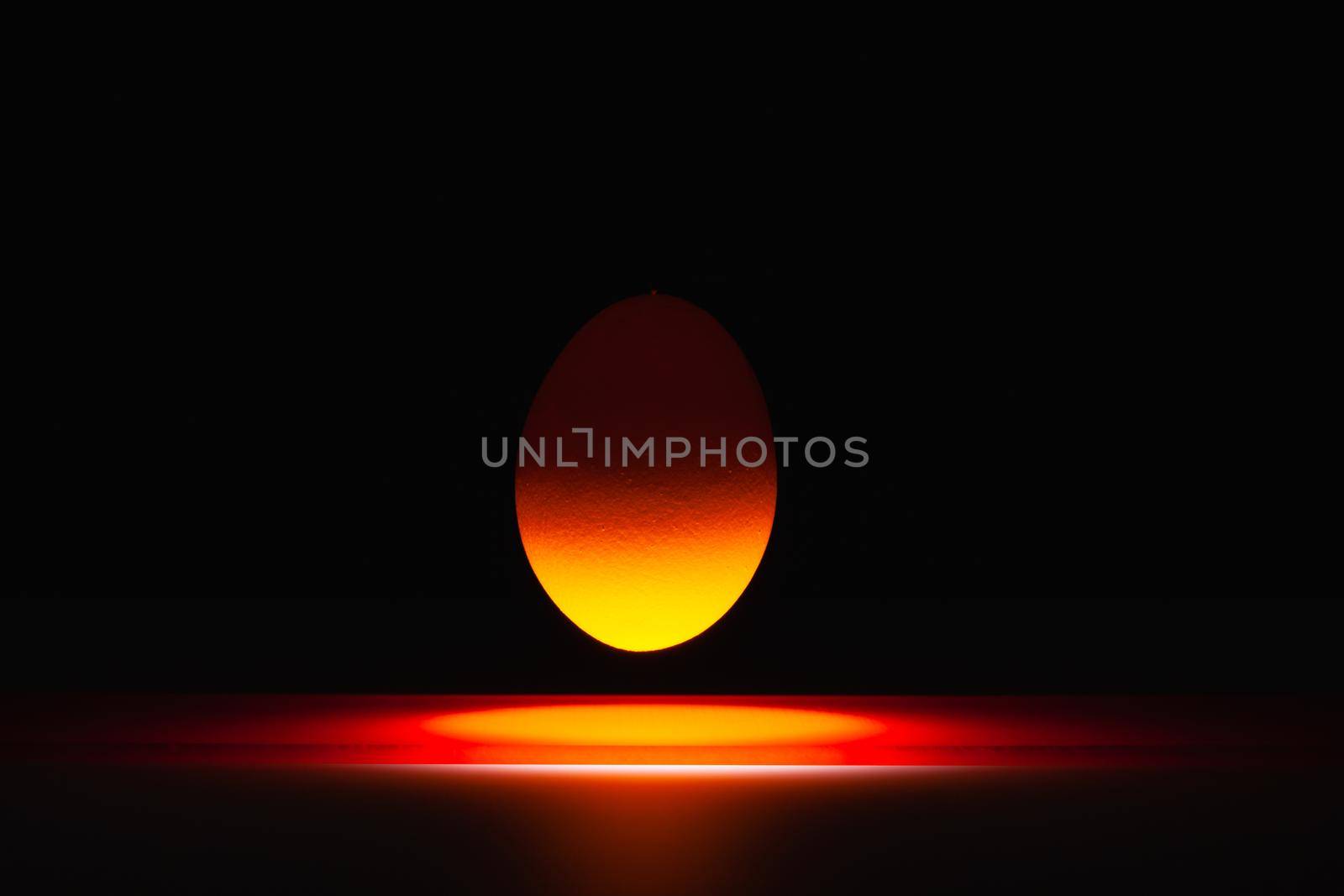 Red egg levitating over a black glass table in the dark room.