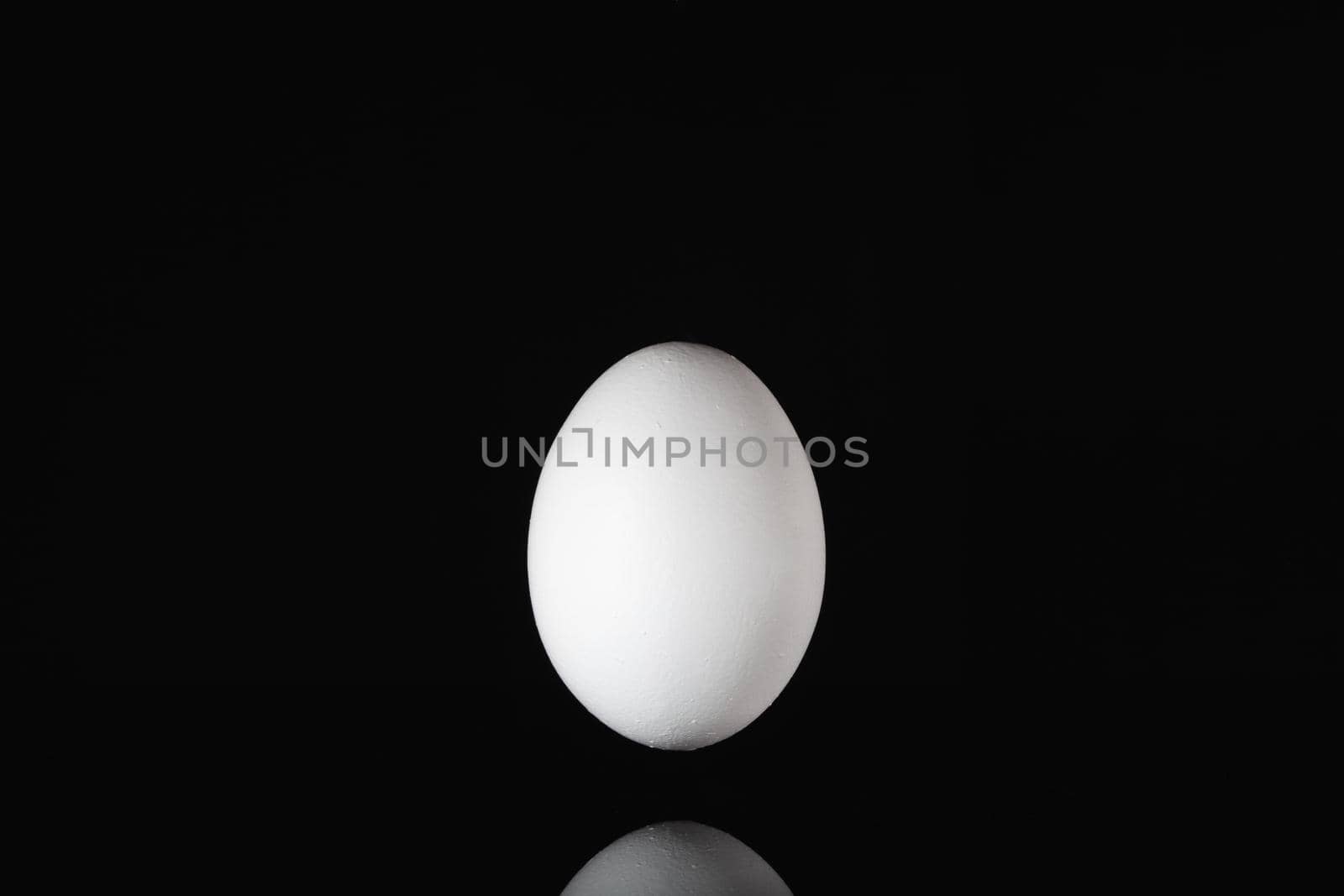 White egg levitating over a black glass table in the dark room.