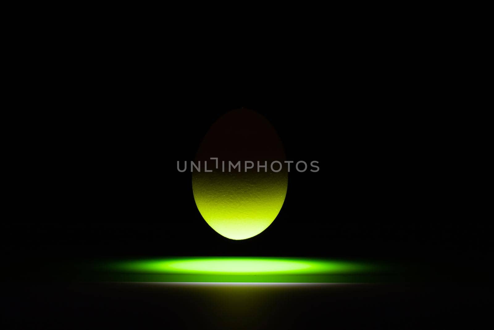 Green egg levitating over a black glass table in the dark room.